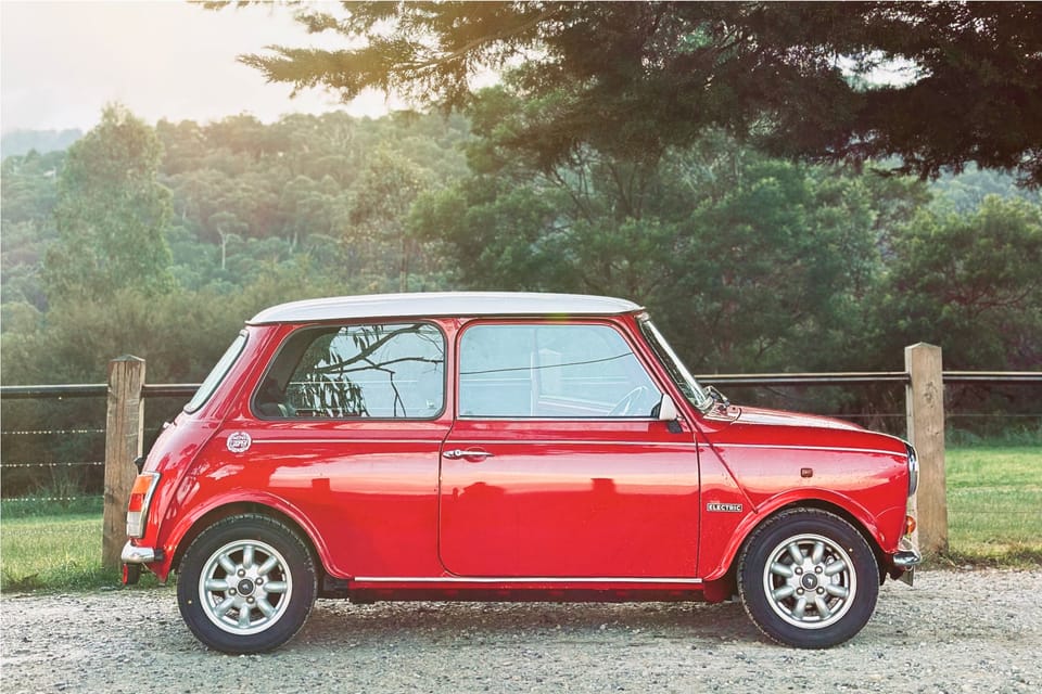 Red Mini with white roof on a country road.