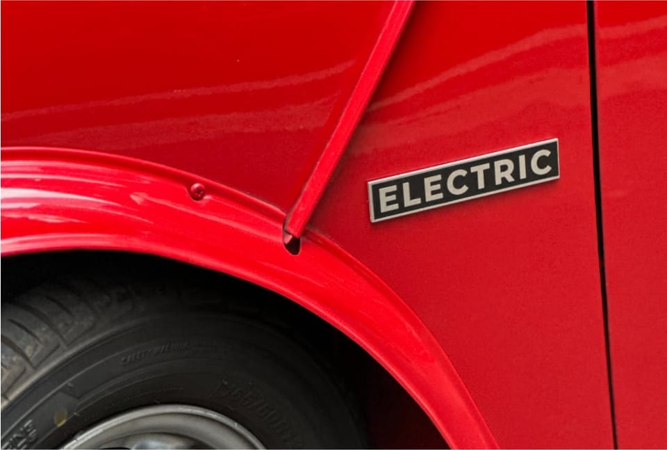 Acid-etched stainless 'electric' badge on the red Mini's wheel arch, where a 1.3 badge used to sit.