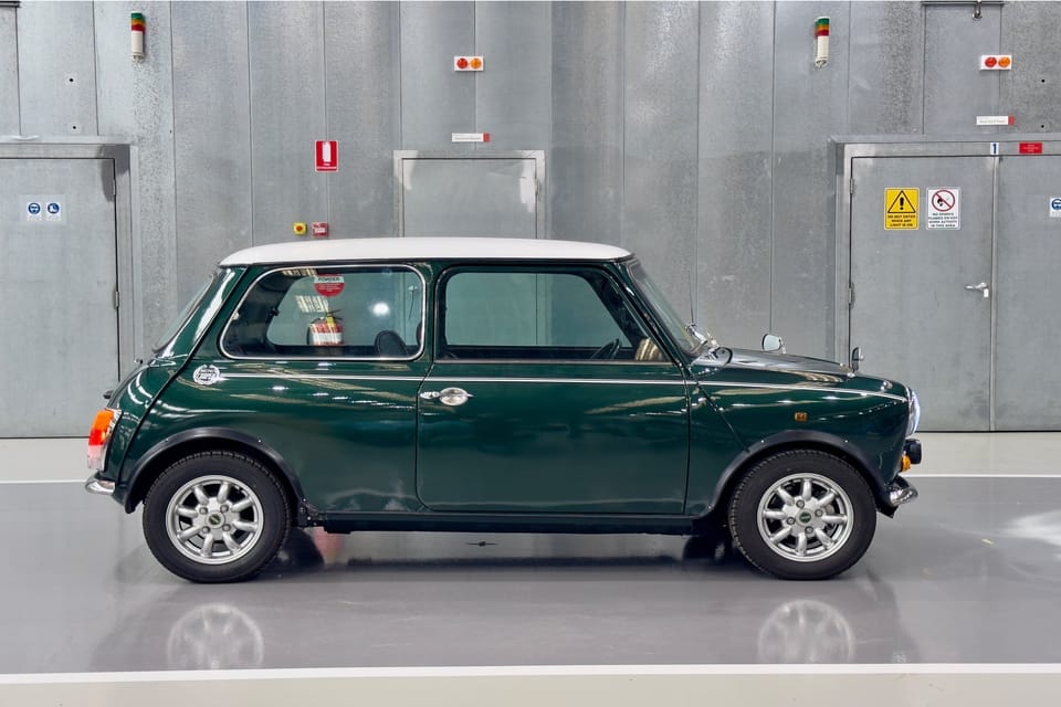 British racing green Classic Mini with a white roof, studio side profile.