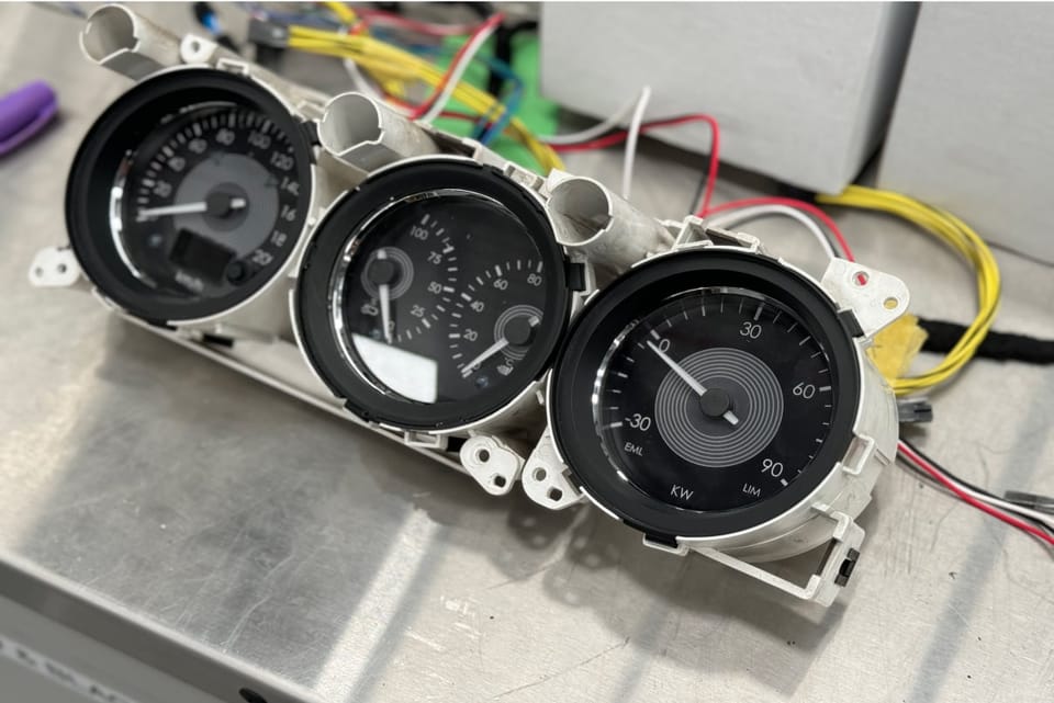 Three-gauge cluster on the bench with wiring behind it.