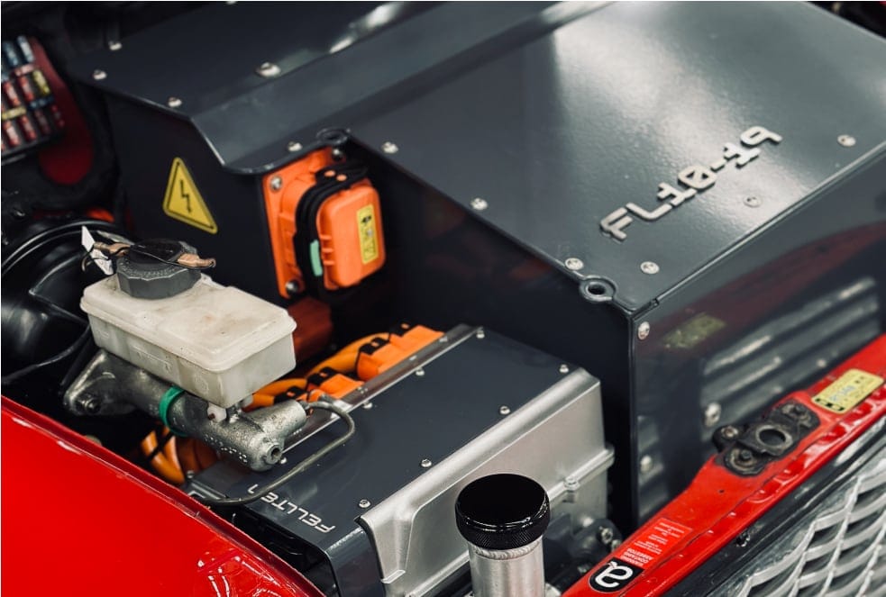 Under the bonnet of the red Mini, the electric drivetrain and orange high-voltage connectors where the petrol four used to be.