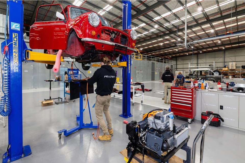 Wide workshop view of the Mini mid-install on the hoist.