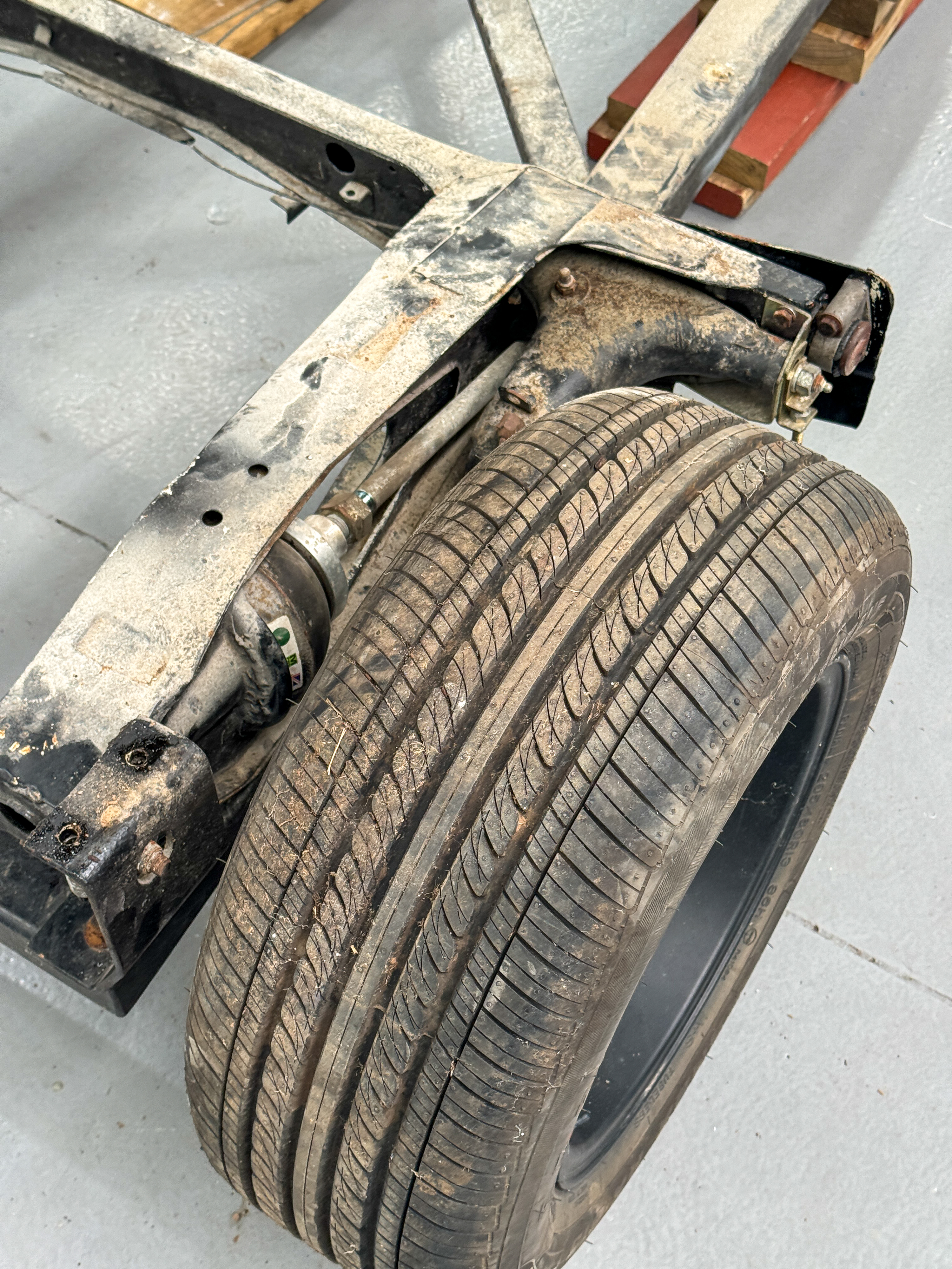 Close view of the original corroded chassis rail and front suspension components on the bare rolling chassis, after sixteen years exposed to coastal weather.