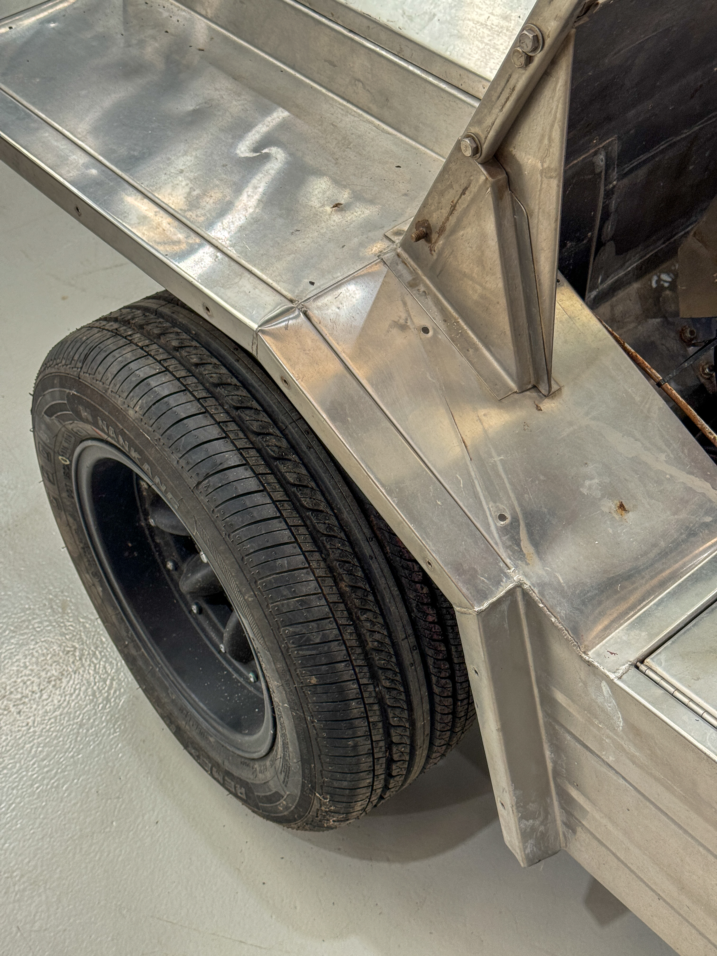 Rear quarter panel of the stainless body before polishing, showing the raw brushed finish with the rear wheel, arch edge, and tub detail visible.