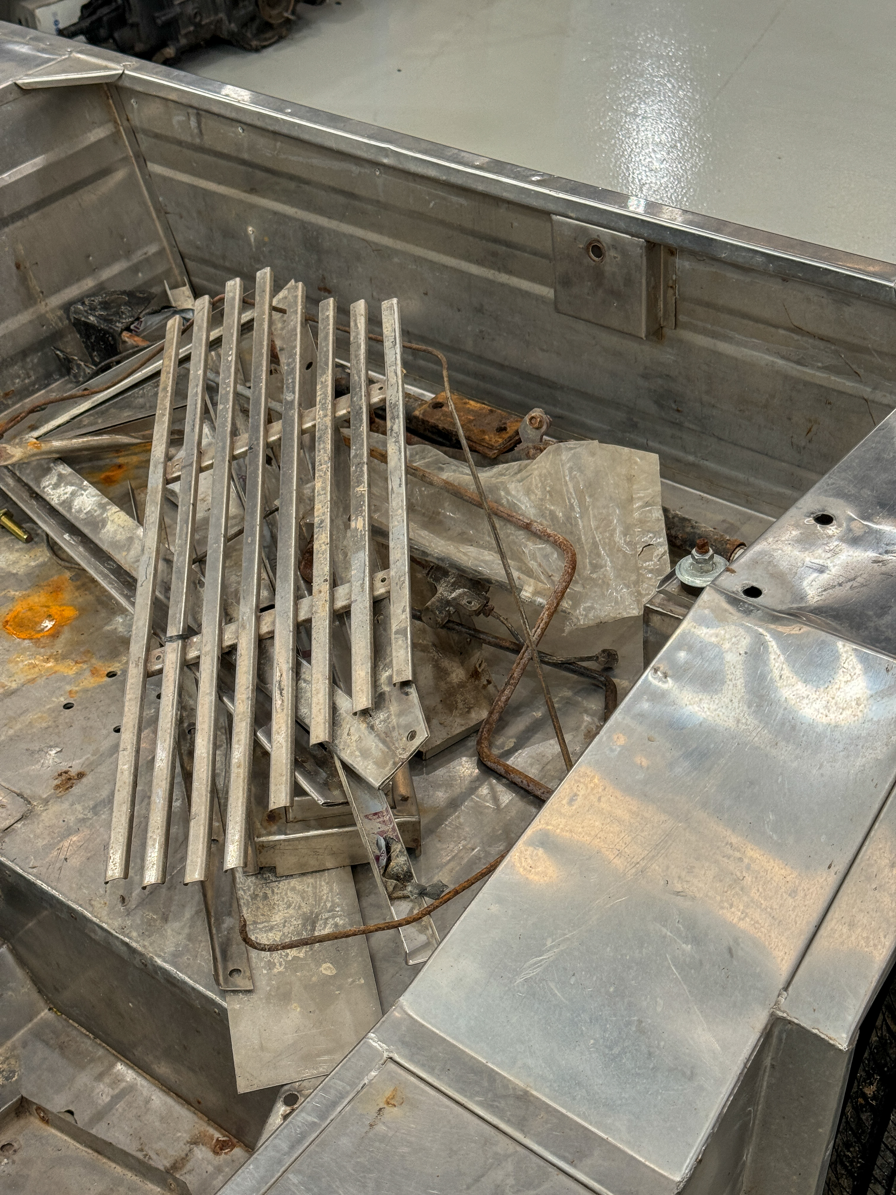 Overhead view of the stripped rear tub with original grille bars and hardware removed and piled inside, showing the raw condition of the body on arrival.