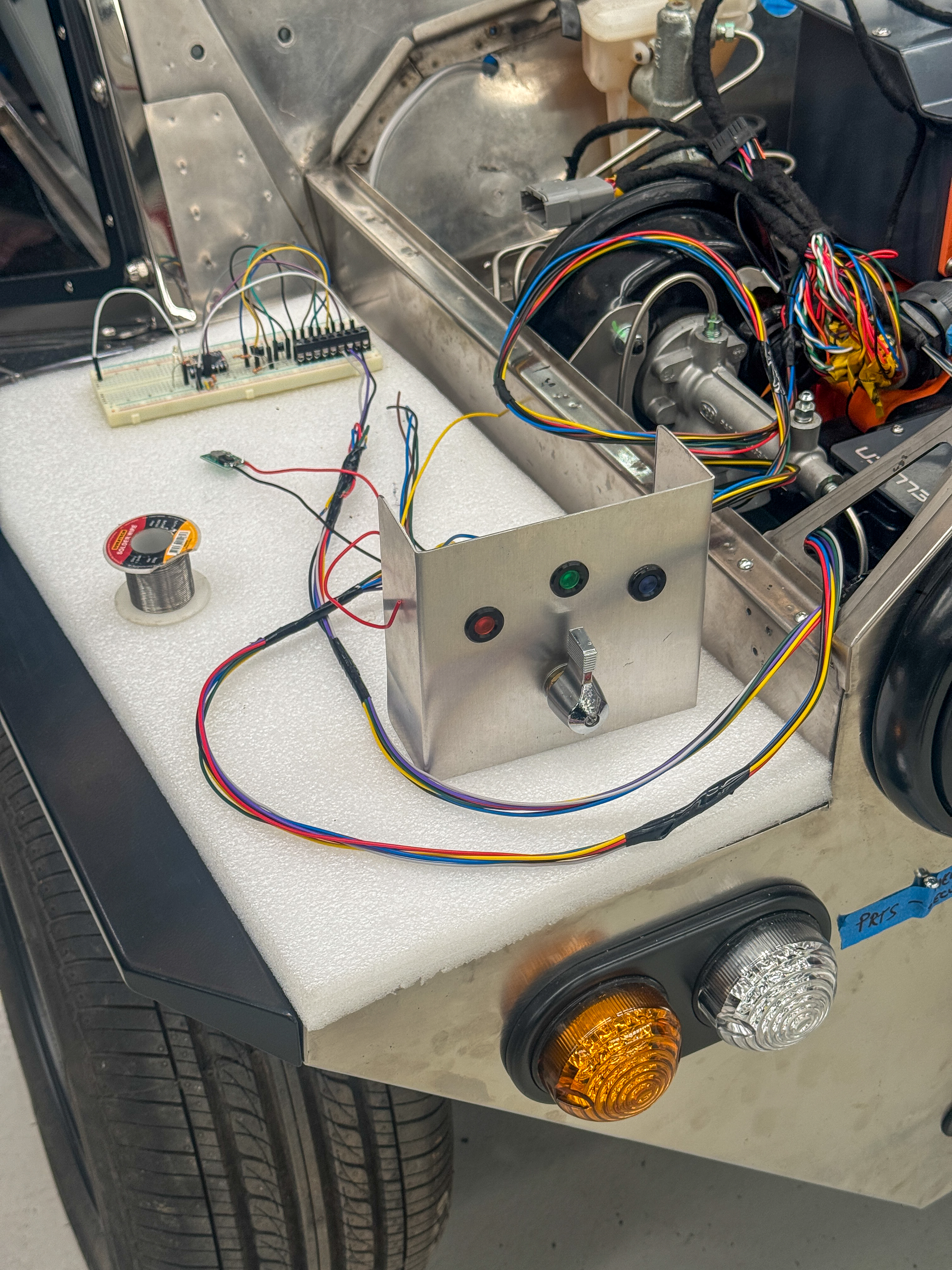 Development wiring loom and breadboard prototype mounted on the rear body panel during electrical system testing, with colourful signal wires and a test switch panel.