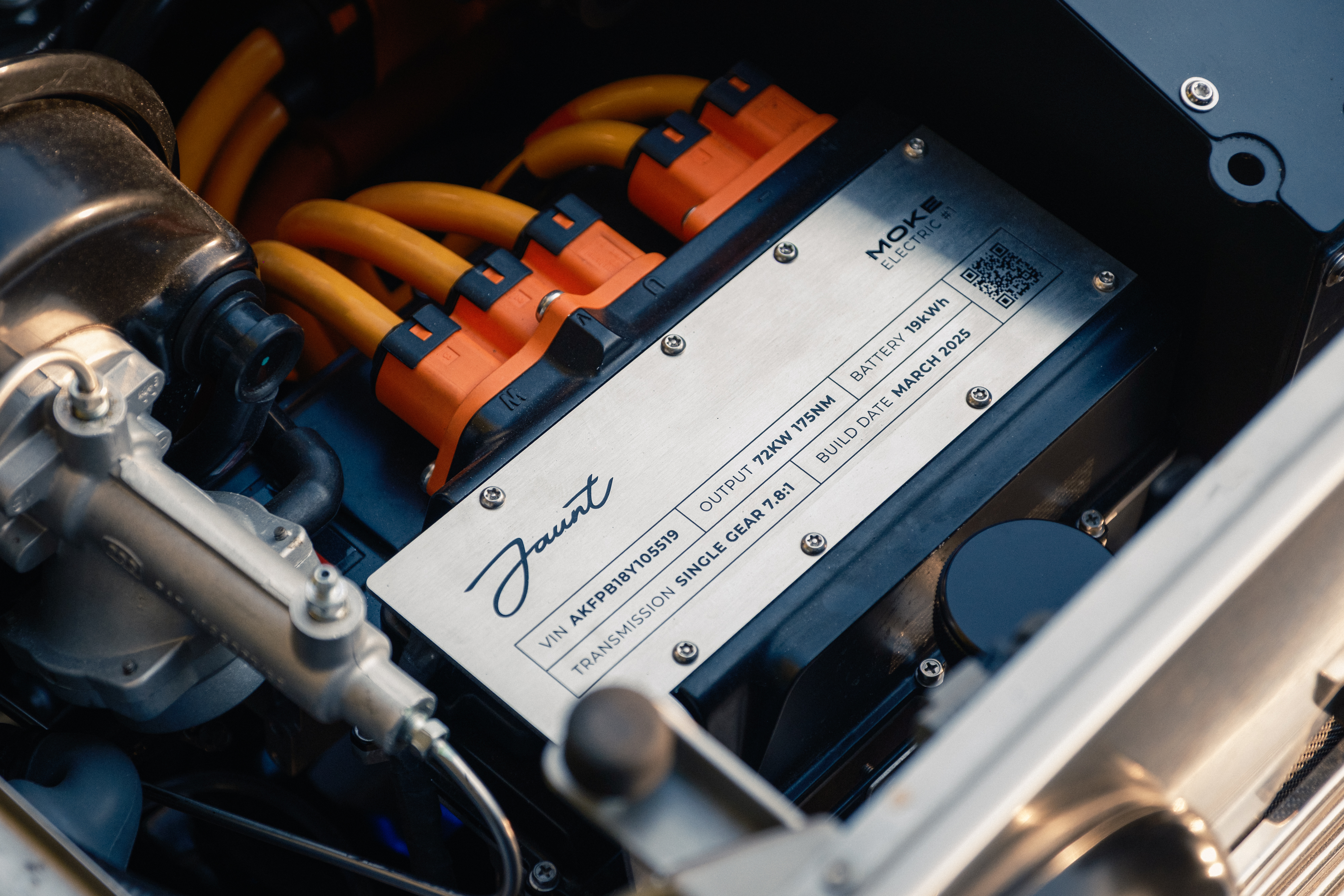 Jaunt build placard inside the electric drivetrain bay showing VIN, 72kW output, 19kWh battery, and March 2025 build date, with orange high-voltage cables above.