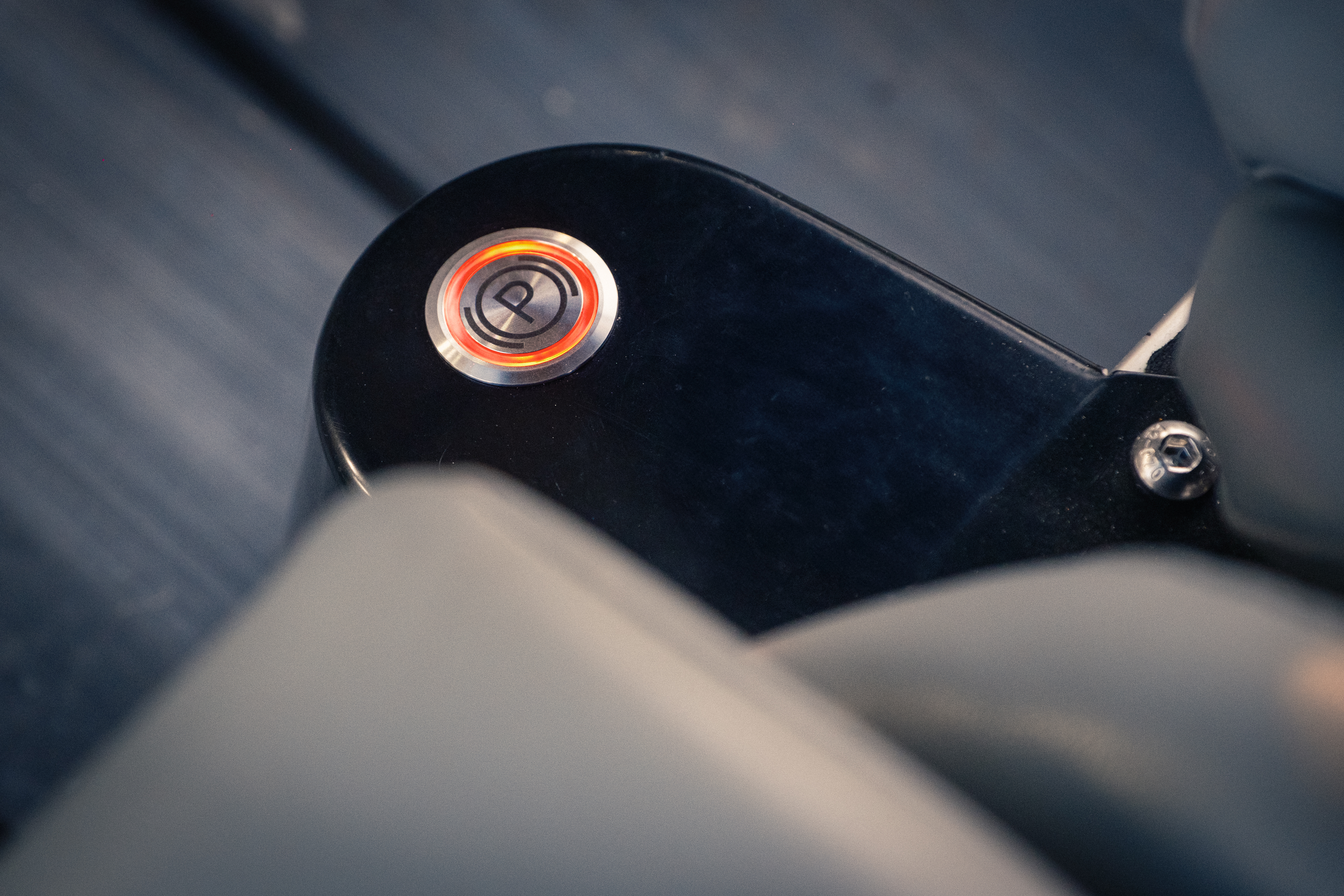 Close-up of the illuminated park button with orange ring glow, set into a black console between the leather seats on the polished stainless tunnel.