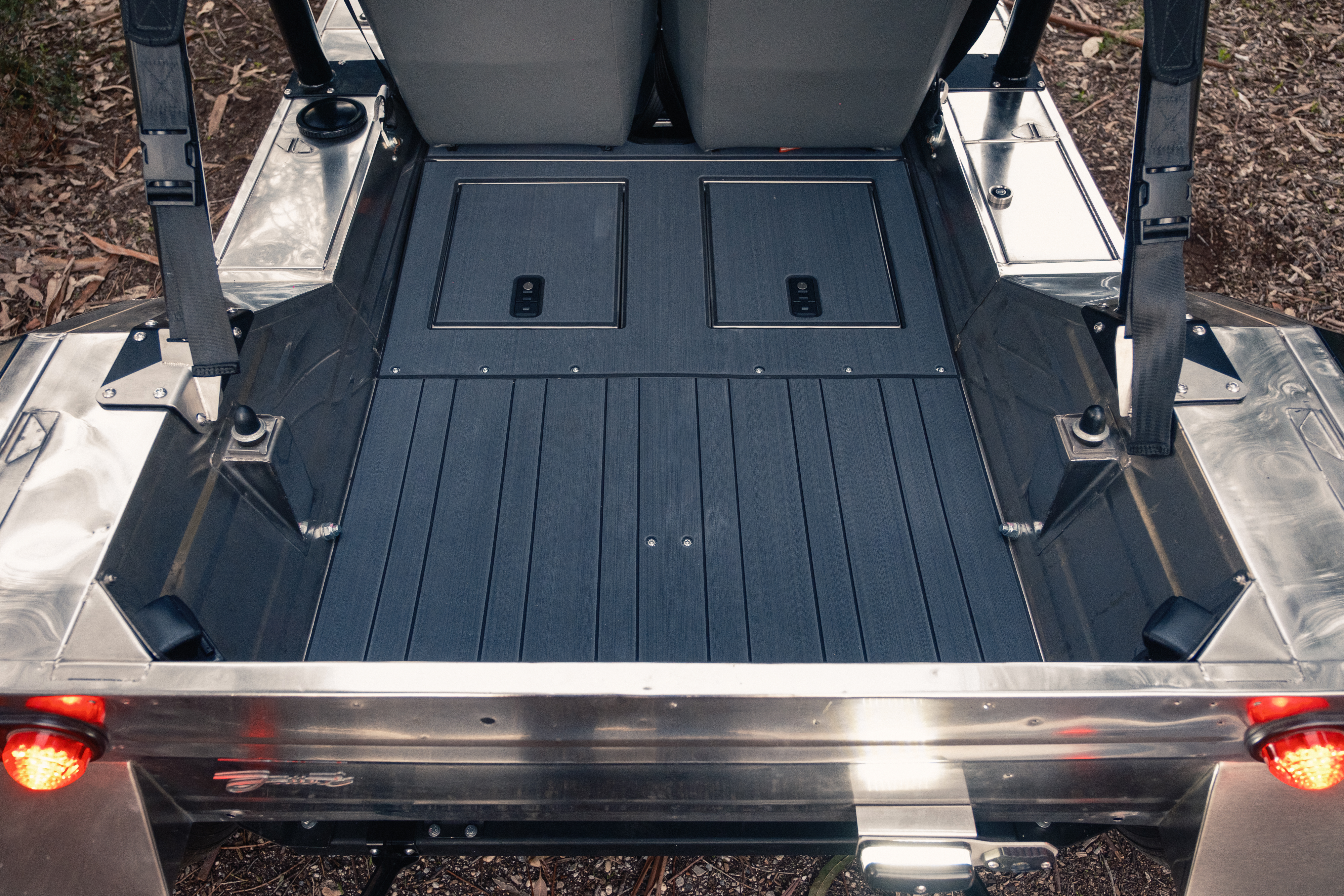 Looking down into the open rear deck tub with a dark composite floor, taillights glowing orange at the base and polished stainless sides framing the cargo area.