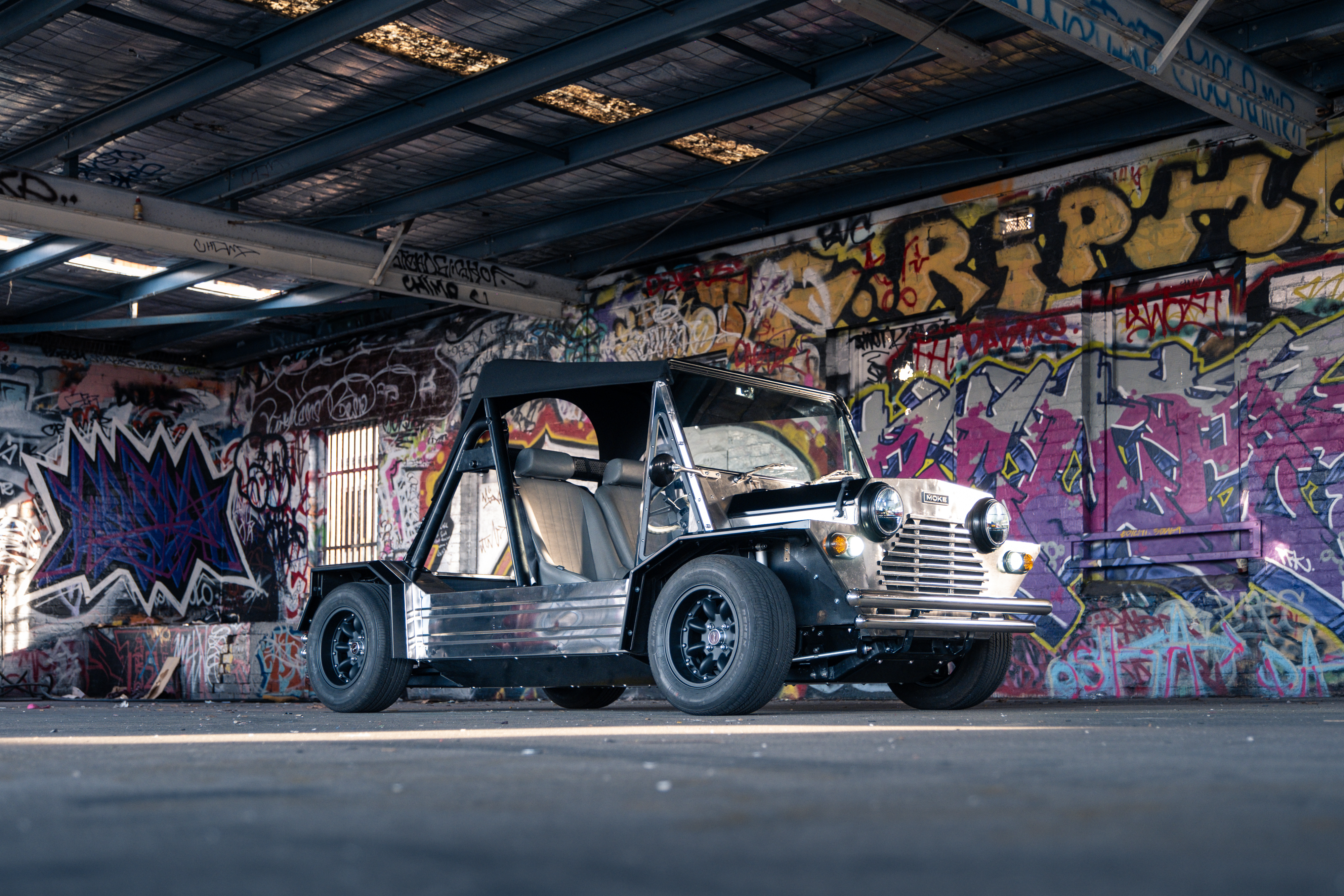Full side profile of the Moke inside an undercover graffiti hall, polished body contrasting sharply with the multi-coloured tags and murals covering every surface.