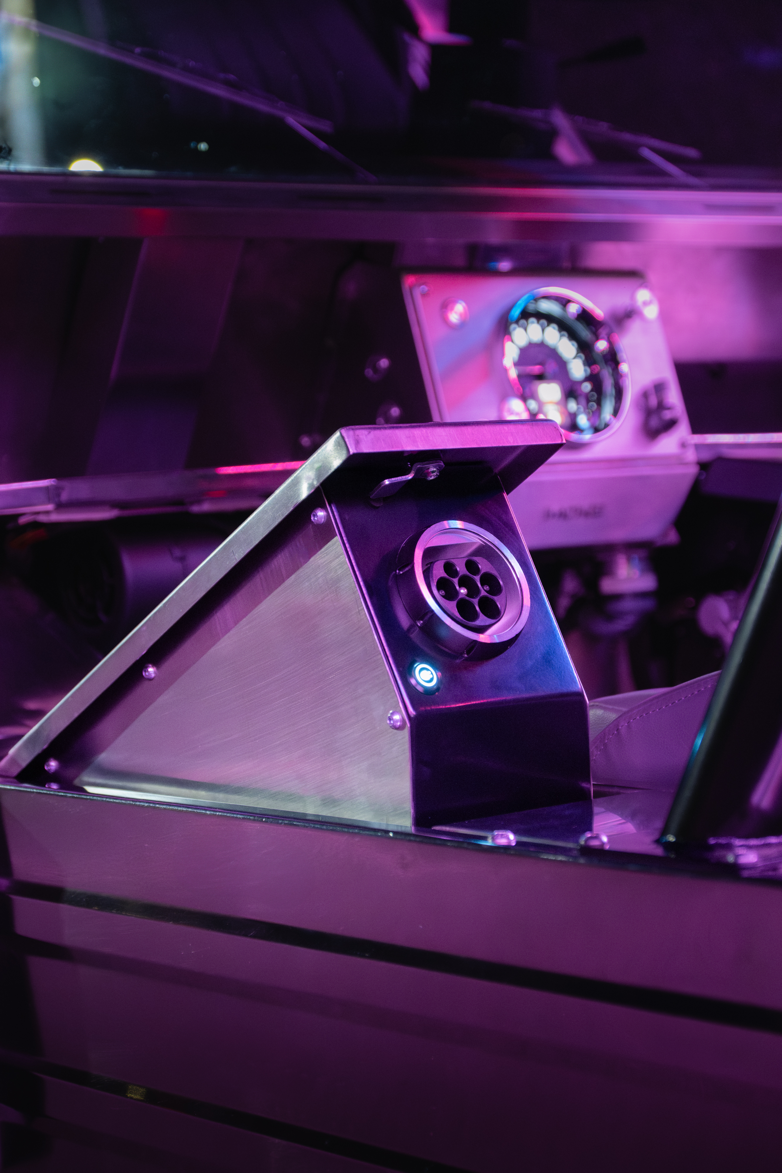 CCS2 charge port revealed in the open side-pod under deep magenta neon, with the glowing charge indicator LED below the socket and the speedometer visible in the background.